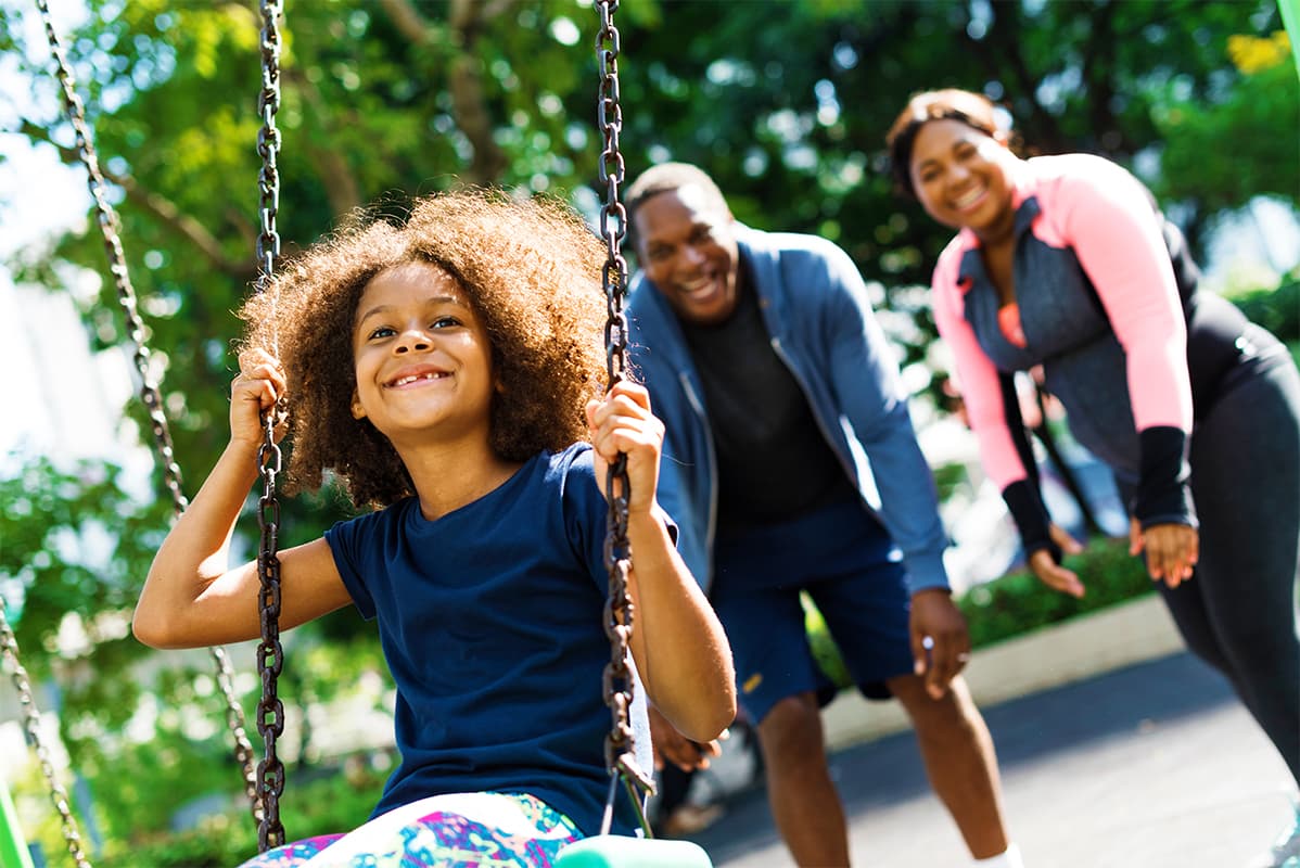 Girl smiling on a swing while her parents smile behind her